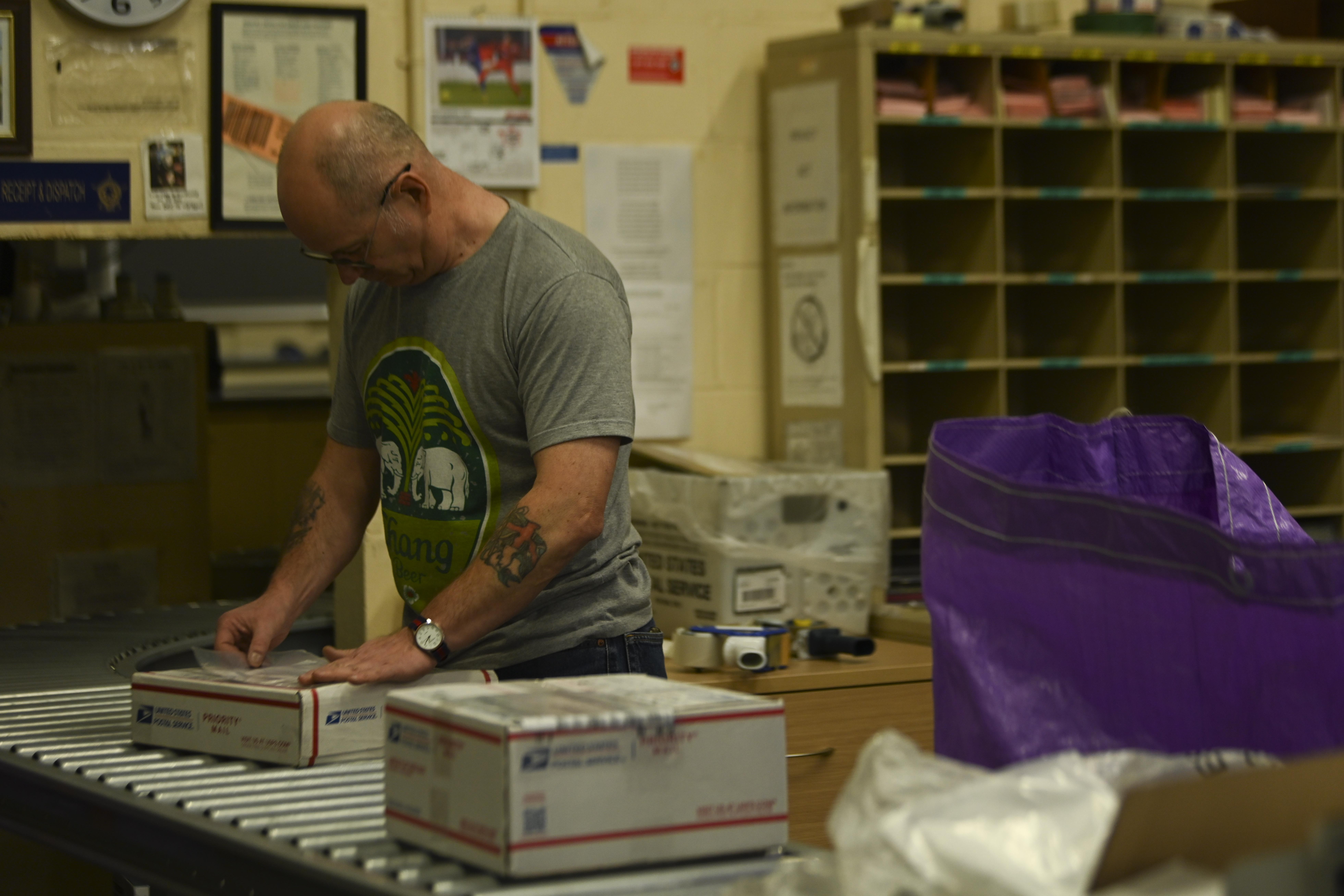 Mark Burrows, 100th Force Support Squadron dispatch worker, places a customs form on an outbound package at the post office at Royal Air Force Mildenhall, England, Dec. 8, 2021. The post office processes personal mail for Airmen and families of Team Mildenhall and official mail for all units across the base. (U.S. Air Force photo by Senior Airman Joseph Barron)