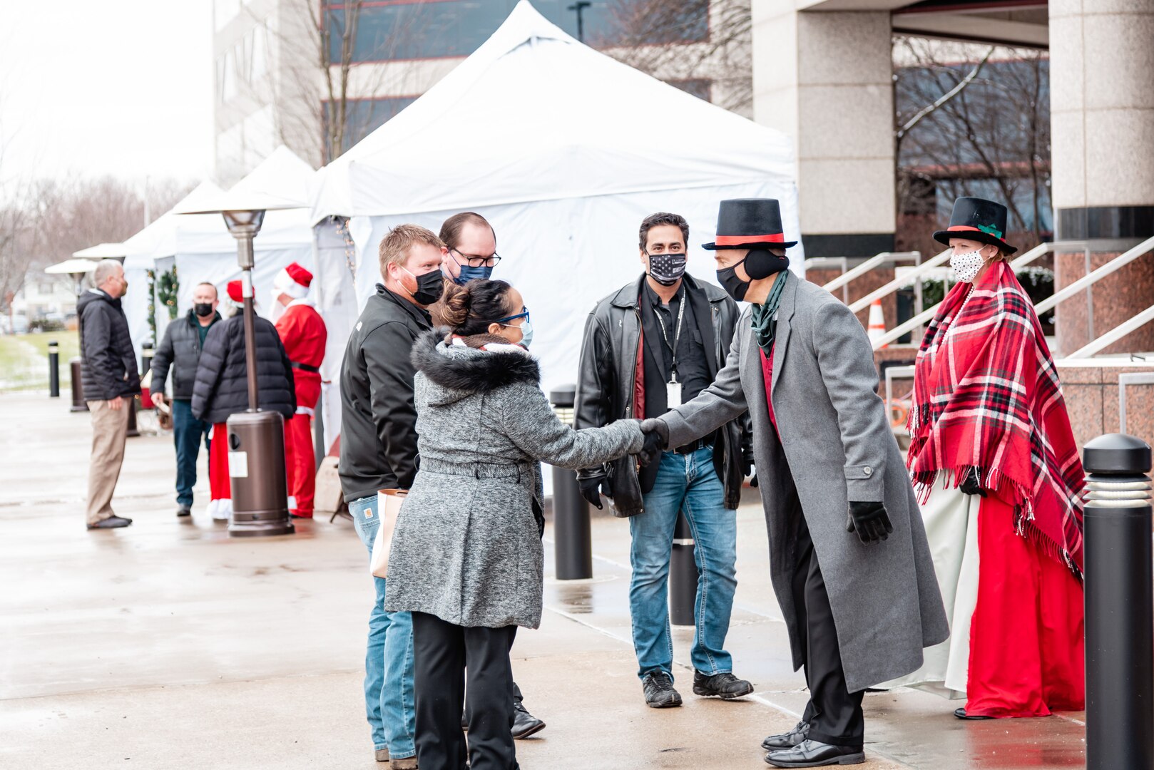 Two people dressed like characters in a Christmas Carol greet people in winter coats outside Building 20.