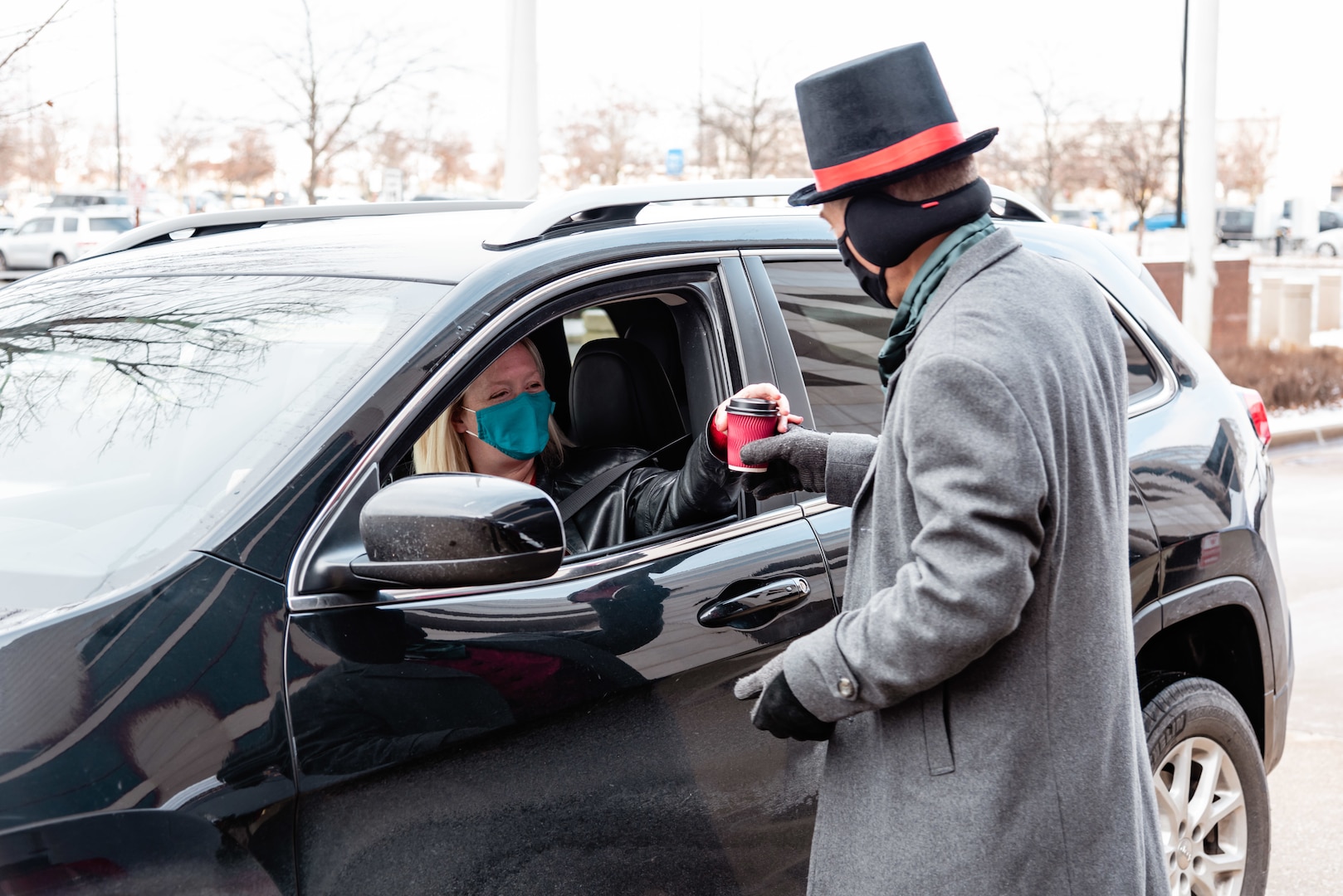 A man dressed like a character in a Christmas Carol hands cider to a woman in a car.