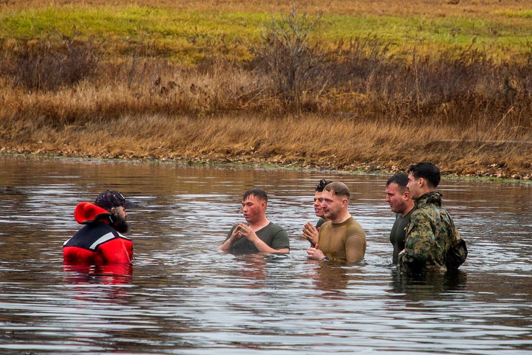 Marines stand in a cold body of water.