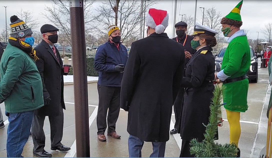 A group of people in military and holiday gear chat with each other outside of Building 20.