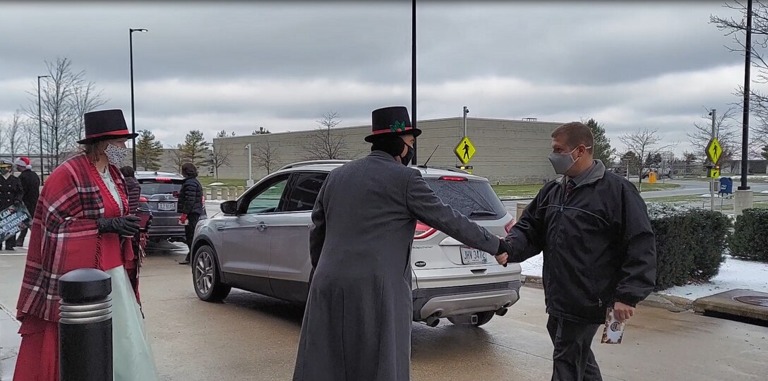 A woman and a man dressed as characters in A Christmas Carol greet a man in a winter jacket.