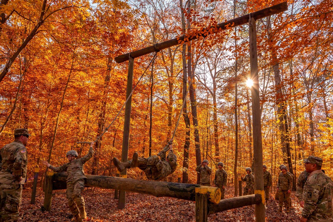 Soldiers participate in an obstacle course in the woods surrounded by colorful leaves.