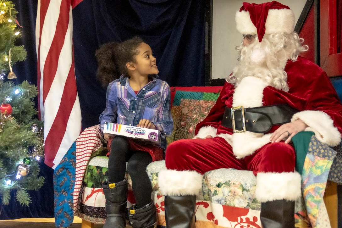 A smiling child talks to a Santa sitting next to her.