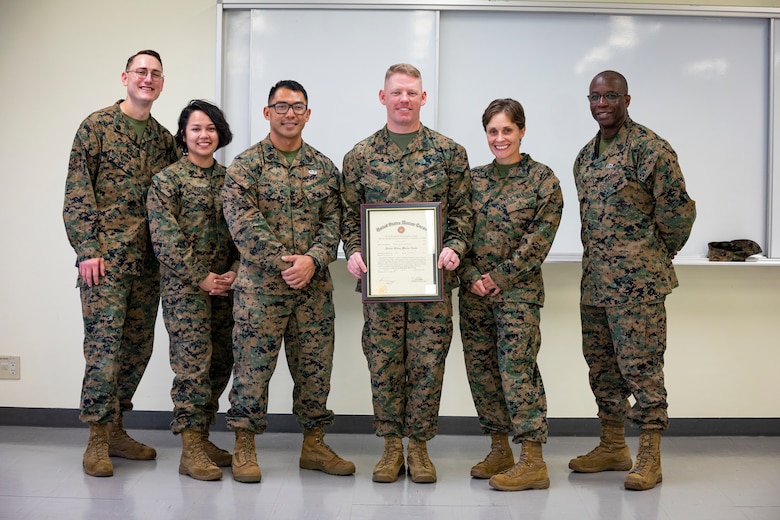 U.S. Marine Corps Gunnery Sgt. Ethan Branch, a career planner with Headquarters and Support Battalion, Marine Corps Installation Pacific, poses with fellow career planners and displays his meritorious promotion warrant after being promoted to gunnery sergeant due to winning the Commandant of the Marine Corps Career Planner of the Year award for 2021 on Camp Foster, Okinawa, Japan, Nov. 19.  Marines nominated for Career Planner of the Year have displayed a consistent high level of performance that significantly and positively impacted mission accomplishment, reflecting exceptional leadership, management and organization skills, devotion to duty, and initiative in support of maintaining a quality enlisted career force. (U.S. Marine Corps photo by Cpl. Karis Mattingly)