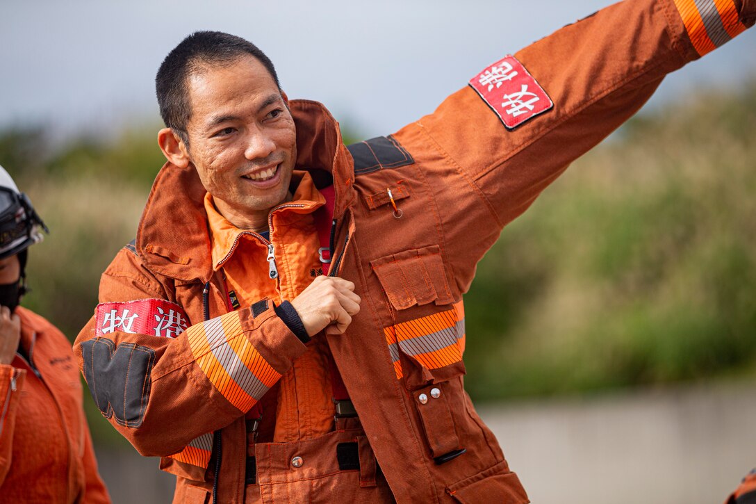 A firefighter with the Urasoe Fire Department Rescue Team applies bunker gear before conducting bilateral live-fire flashover training on Camp Hansen, Okinawa, Japan, Dec. 7, 2021. The training between Marine Corps Installations Pacific Fire and Emergency Services and the Urasoe Fire Department Rescue Team began with an instructional period in which the local community firefighters were introduced to emergency fire response tactics practiced in the U.S. After the class, firefighters from both departments put on their safety gear and entered into an enclosed fire laboratory, known as the Swede Survival Phase 1 System, to observe the dynamics of a common fire which transitions into a flashover, a near-simultaneous ignition of most of the directly combustible material inside an enclosed area. (U.S. Marine Corps photo by Lance Cpl. Alex Fairchild)