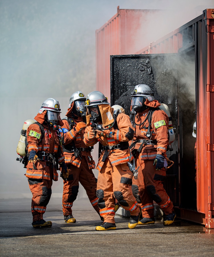 Firefighters with the Urasoe Fire Department Rescue Team exit a Swede Survival Phase 1 System during bilateral live-fire flashover training on Camp Hansen, Okinawa, Japan, Dec. 7, 2021. The training between Marine Corps Installations Pacific Fire and Emergency Services and the Urasoe Fire Department Rescue Team began with an instructional period in which the local community firefighters were introduced to emergency fire response tactics practiced in the U.S. After the class, firefighters from both departments put on their safety gear and entered into an enclosed fire laboratory, known as the Swede Survival Phase 1 System, to observe the dynamics of a common fire which transitions into a flashover, a near-simultaneous ignition of most of the directly combustible material inside an enclosed area. (U.S. Marine Corps photo by Lance Cpl. Alex Fairchild)