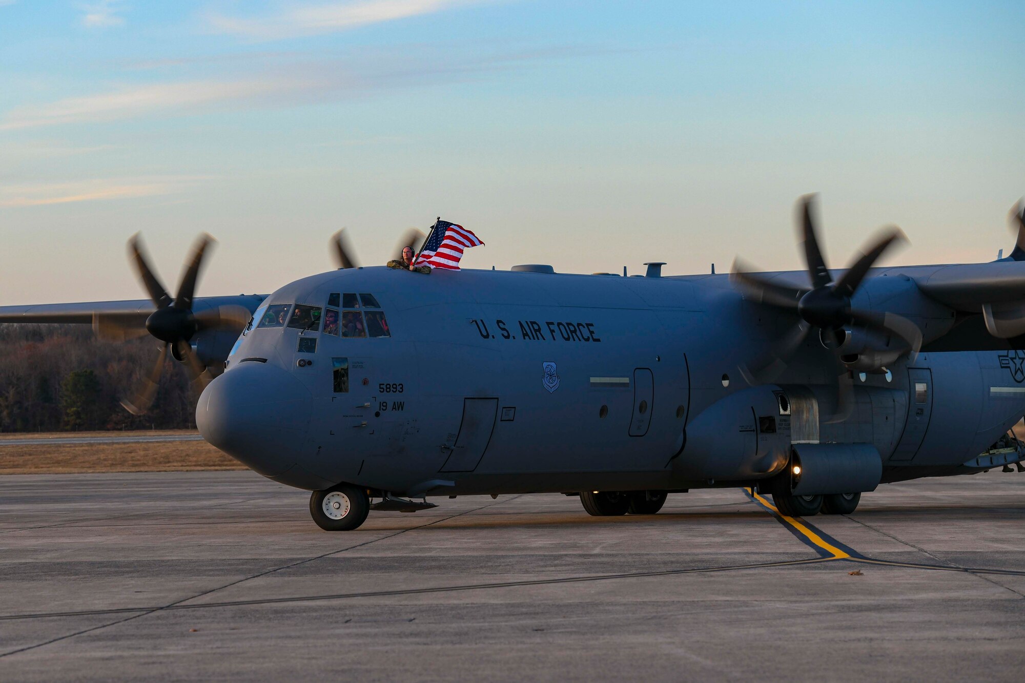 An Airman waves a flag on top of a C-130.