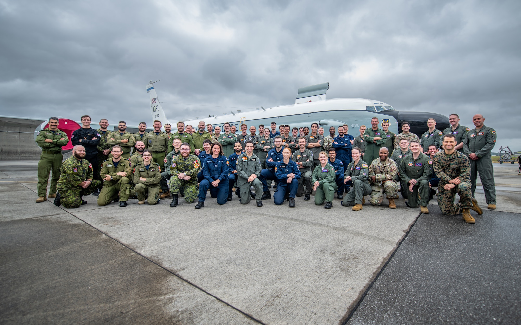 A group of military members from the U.S., New Zealand and Canada all pose for a photo in front of a plane