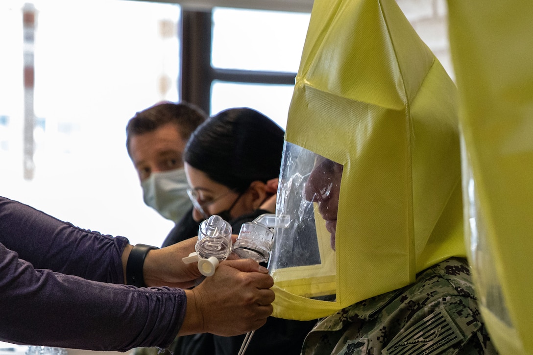 A soldier is fitted for a N95 mask while two other soldiers wearing face masks wait their turn.