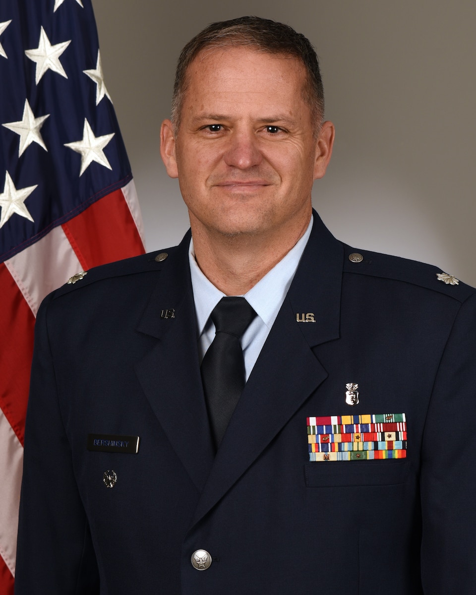 Official photo of a man in service dress in front of a portion of the American flag.
