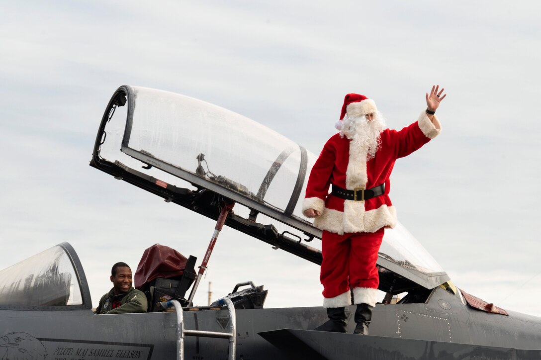 Santa Claus waves while standing on an aircraft.