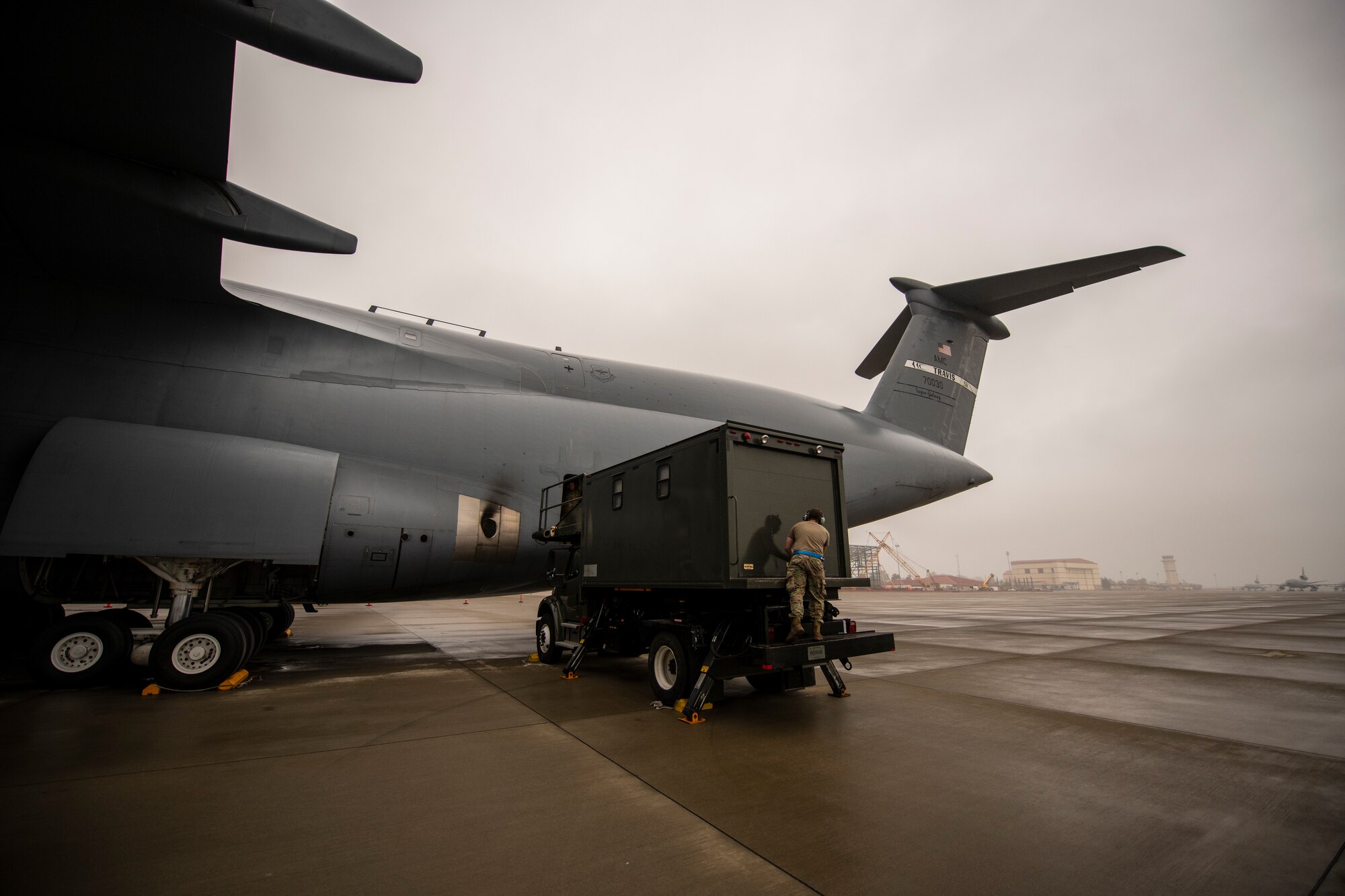 A large maintenance truck is parked next to a very large grey military aircraft.