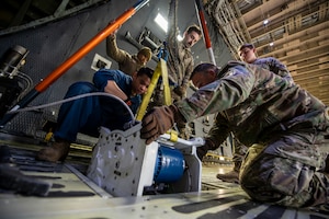 A wide show of a warehouse with men in military uniform working on a piece of machinery with rope on it.