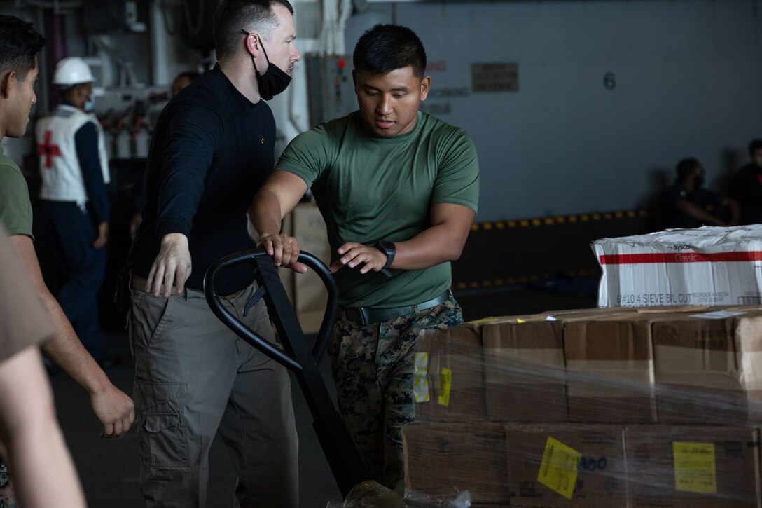A U.S. Marine works with other Marines and Sailors to move containers of food and supplies, during a replenishment at sea (RAS), aboard amphibious assault ship USS Kearsarge (LHD 3), Dec. 11, 2021. RAS is conducted to transfer necessities such as munitions, supplies, and food from one ship to another while underway. (U.S. Marine Corps photo by Cpl. Yvonna Guyette)