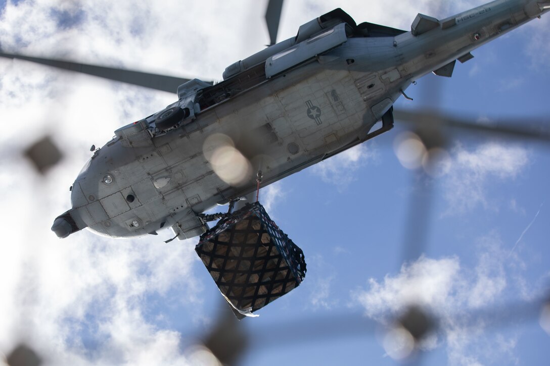 U.S. Navy pilots with Helicopter Sea Combat Squadron 28, transport supplies from USNS Leroy Grumman (T-AO-195), using MH-60S Seahawk Helicopters during a replenishment at sea (RAS), aboard amphibious assault ship USS Kearsarge (LHD 3), Dec. 11, 2021. RAS is conducted to transfer necessities such as munitions, supplies, and food from one ship to another while underway. (U.S. Marine Corps photo by Cpl. Yvonna Guyette)