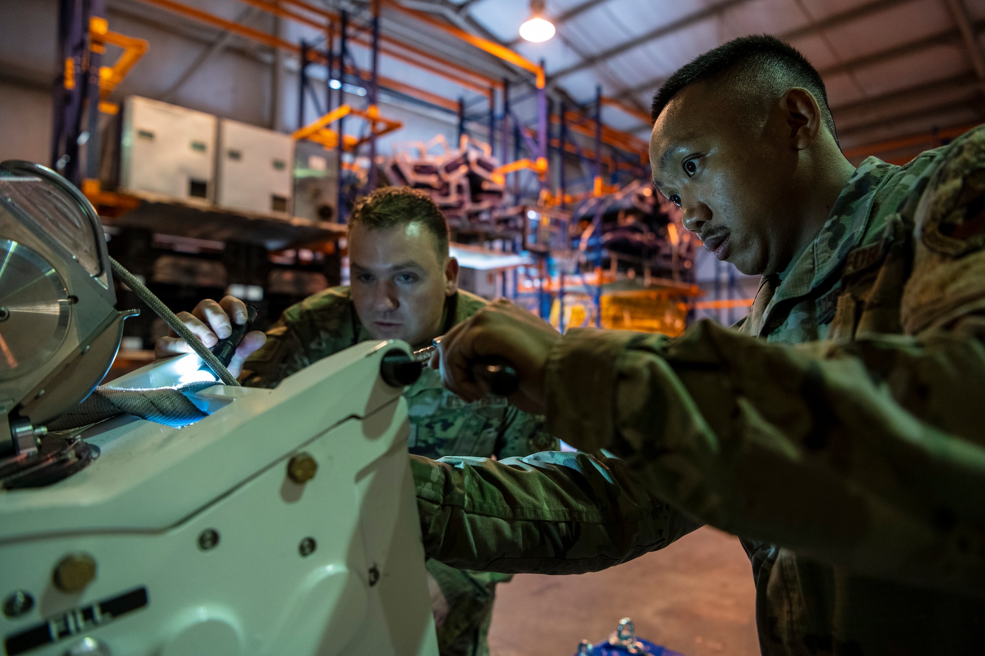 Two men in military uniform look at a machine that has a rope and pully system attached.