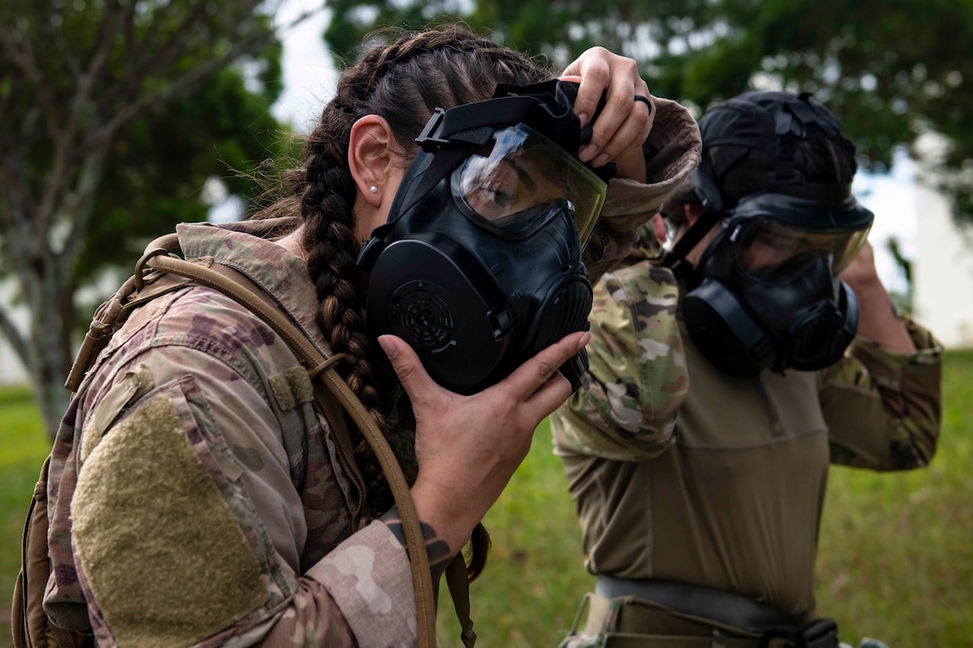 Two airmen put on gas masks.