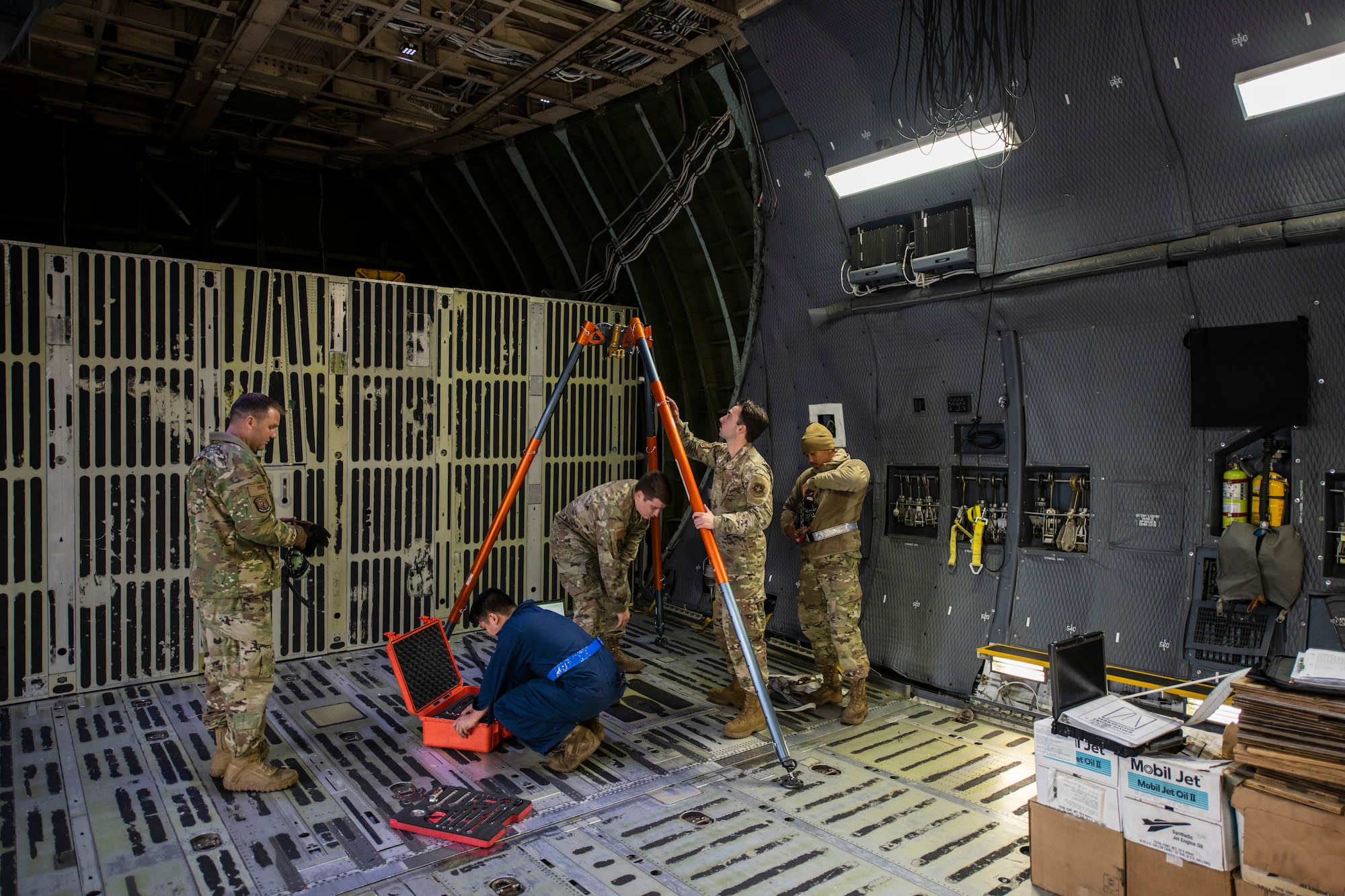 Men in uniform are preparing to replace a piece of machinery with rope on a large military aircraft.