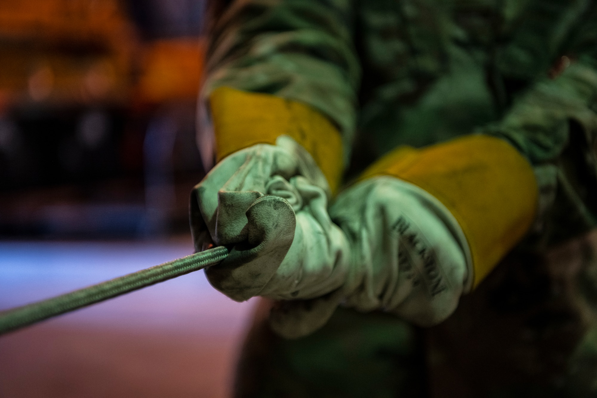 A rope is being pulled through the hands of a man in gloves and military uniform.