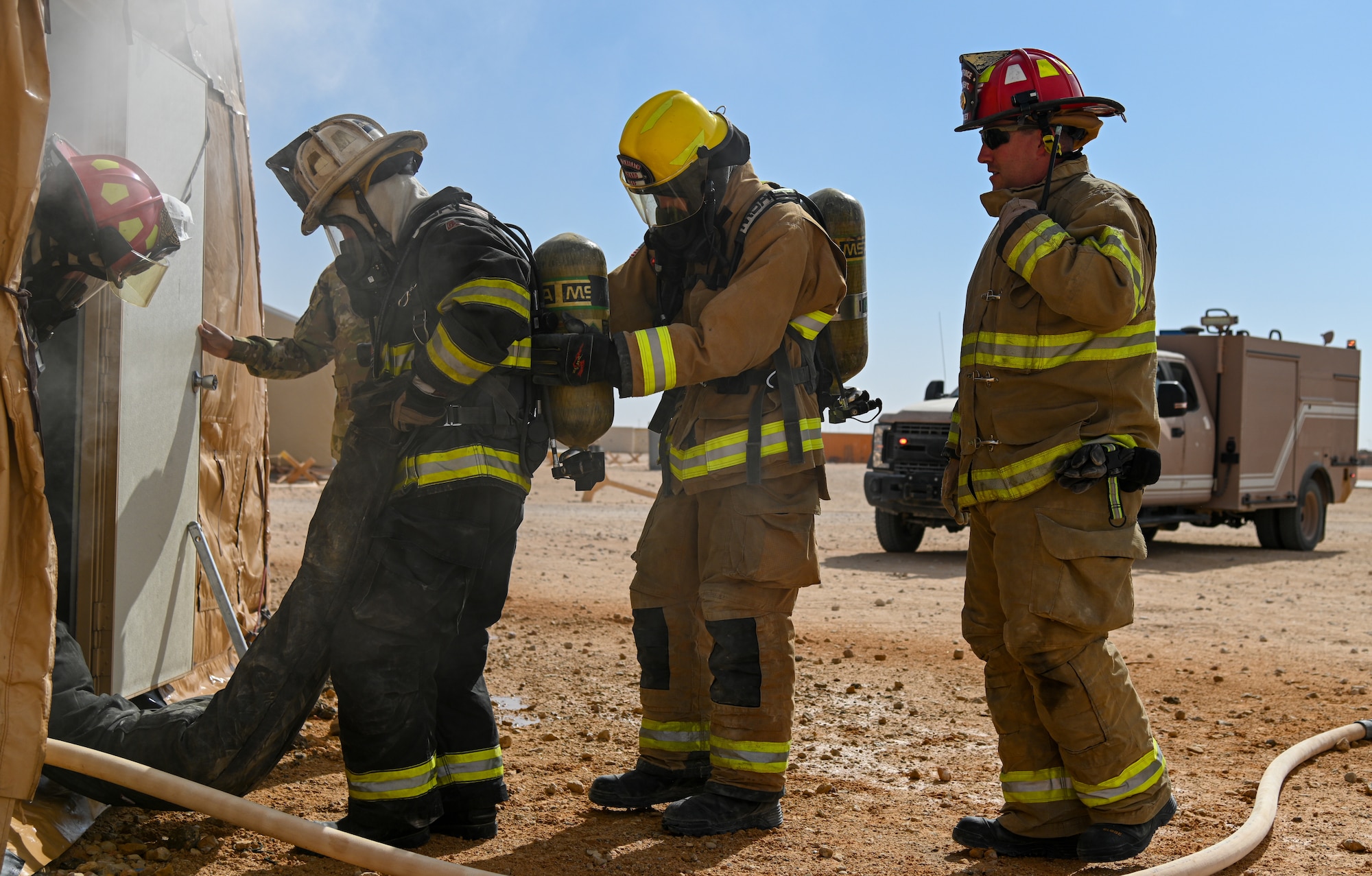 U.S. Air Force Brig. Gen. Robert Davis, second from the left, 378th Air Expeditionary Wing commander, simulates extracting personnel from a structure fire alongside members of the 378th Expeditionary Civil Engineer Squadron  at Prince Sultan Air Base, Kingdom of Saudi Arabia, Dec. 9, 2021. Members of the 378th ECES taught Davis how to don a complete fire suit as well as how to properly extinguish a structure fire. (U.S. Air Force photo by Staff Sgt. Christina Graves)