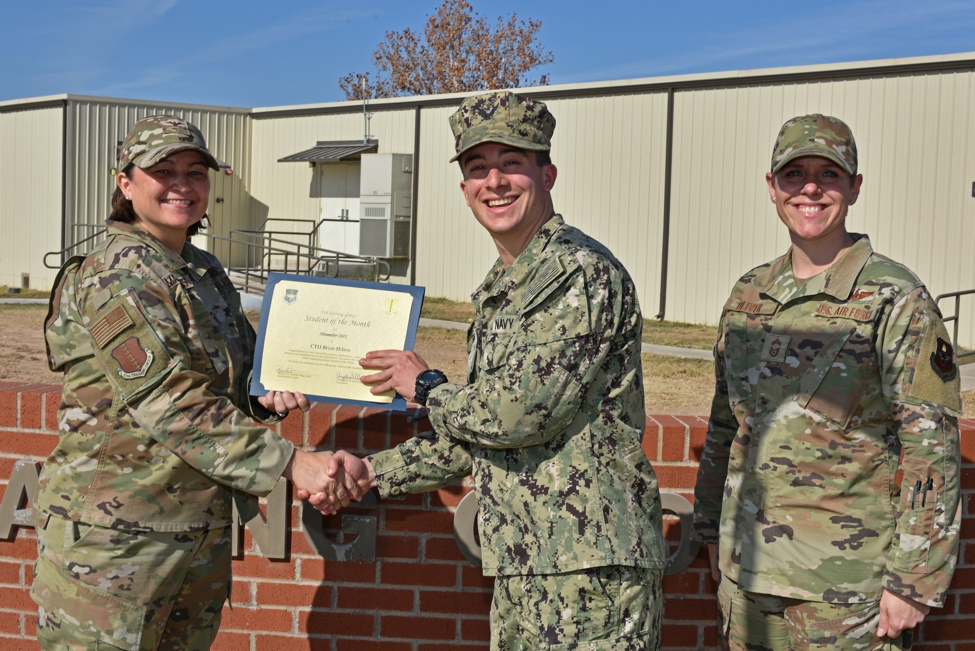 U.S. Air Force Col. Angelina Maguinness, 17th Training Group commander, and Chief Master Sgt. Breana Oliver, 17th TRG superintendent, present U.S. Navy Petty Officer 3rd Class Brian Hilten, 316th Training Squadron student, the 316th TRS Student of the Month award for November 2021, on Goodfellow Air Force Base, Texas, Dec. 14, 2021. The 316th TRS is responsible for training, developing, and inspiring intelligence surveillance and reconnaissance cryptologic leaders. (U.S. Air Force photo by Senior Airman Ashley Thrash)