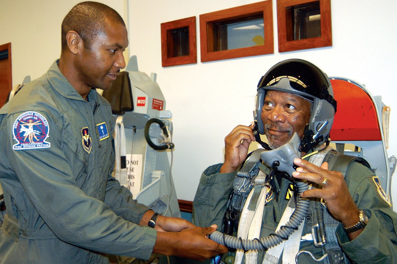 An airman holds a breathing tube for a man in a flight suit.