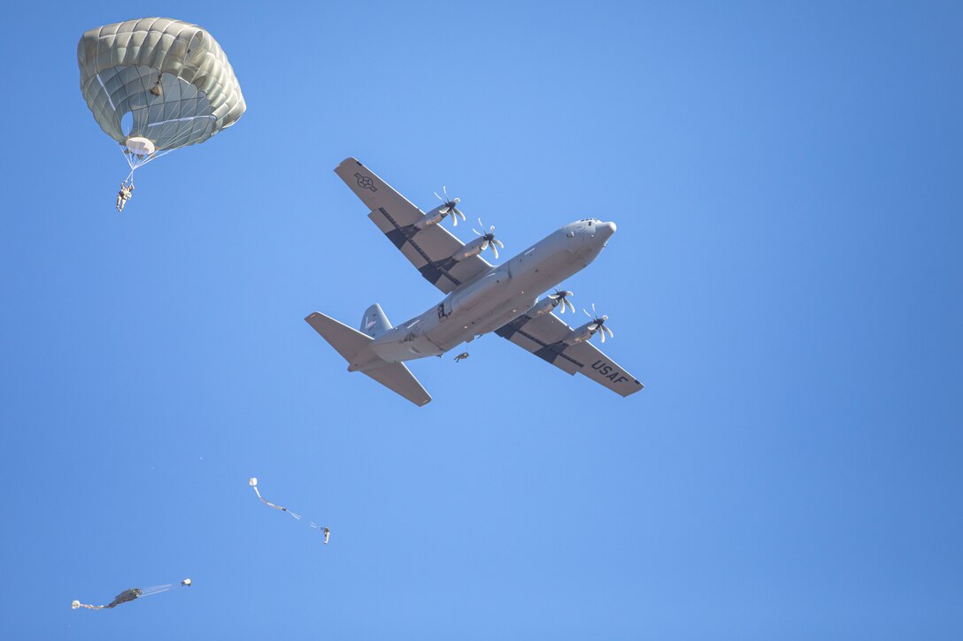 Parachutists descend by an aircraft flying in blue sky.