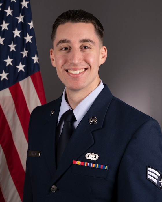 Official Photo of SrA Brian Galaviz, guitarist with Full Spectrum, one of six ensembles in the Heritage of America Band, Langley AFB, VA.  SrA Galaviz is wearing blue service dress in front of the American flag.