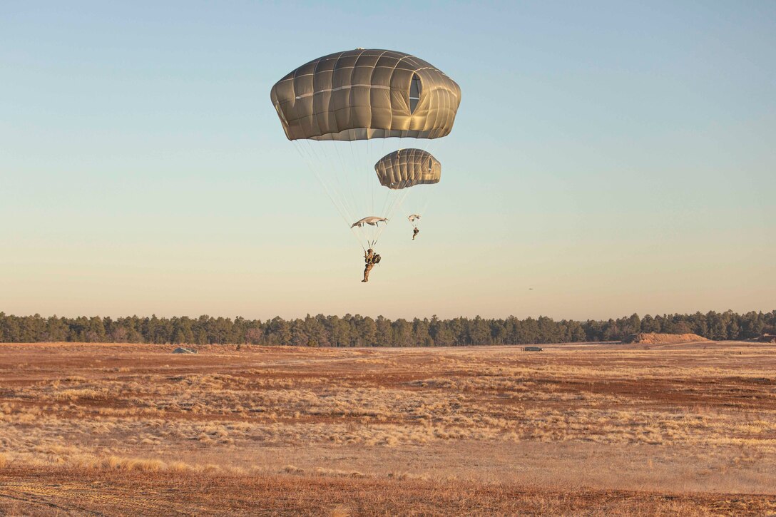 Two soldiers descend in the air wearing parachutes.