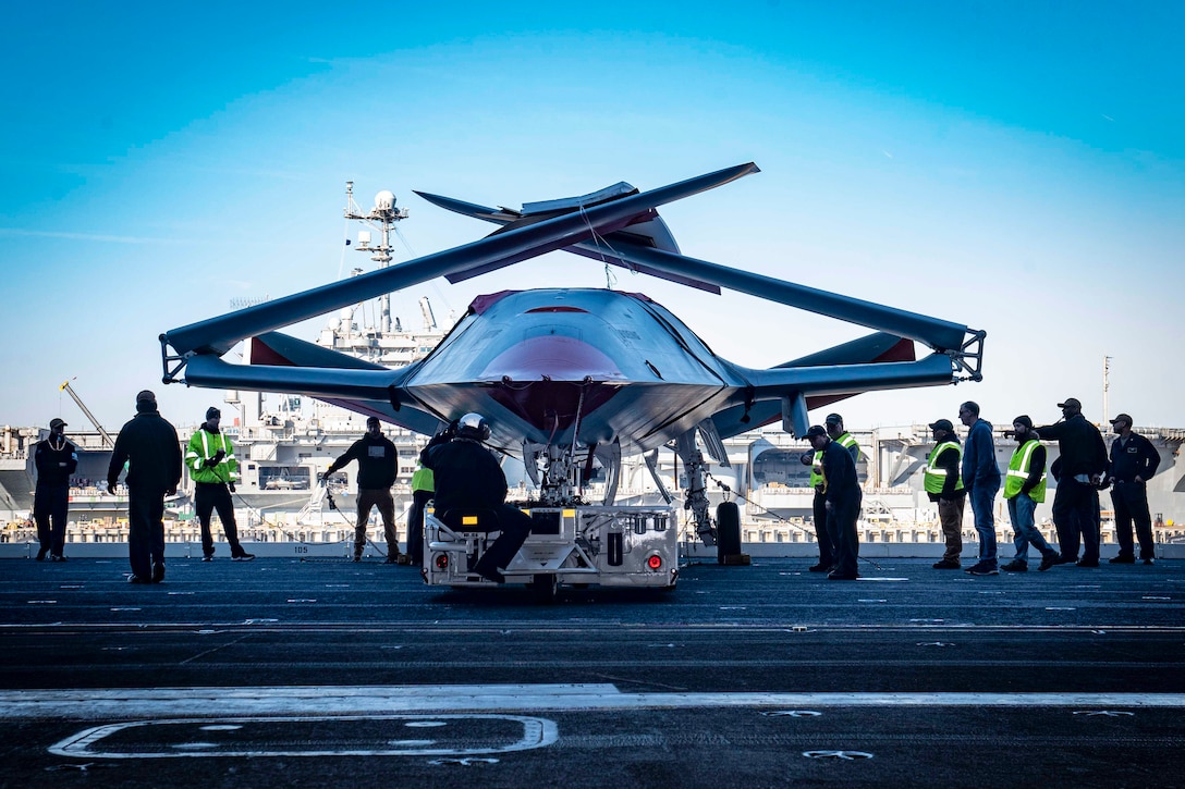Sailors and civilians work around an unmanned aircraft on a ship's flight deck.