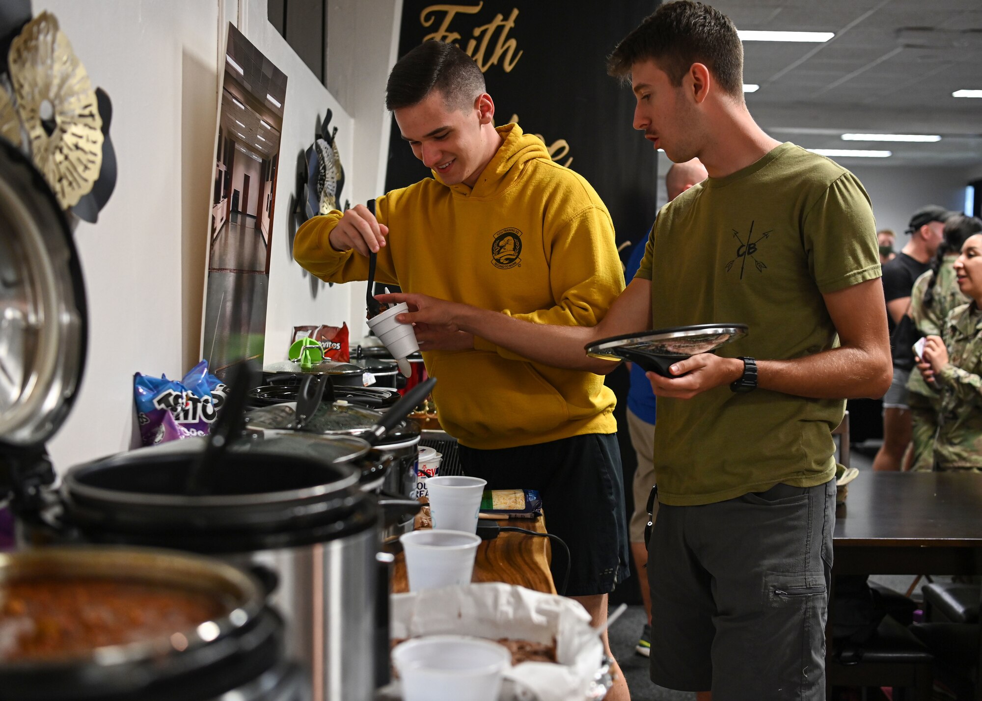 Two U.S. Air Force Airmen assigned to Andersen Air Force Base, Guam, get a scoop of chili during a chili cook off at an opening ceremony of an Airmen’s Center at Chapel 1, Andersen Air Force Base, Guam, Dec. 15, 2021. Members from the chapel team and dorm residents worked for months reconstructing an empty space to operationalize a piece of the chapel to be Airmen focused. (U.S. Air Force photo by Senior Airman Aubree Owens)