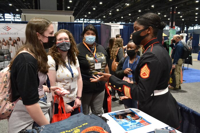U.S. Marine Staff Sgt. Mardia A. Timoney,  a musician technical assistant with 6th Marine Corps District, speaks with attendees at the Midwest Clinic International Band, Orchestra, and Music Conference in Chicago, Dec. 15, 2021.  Marine Corps Recruiting Command Marines take part in this annual event in order to connect with various music professionals through performances and clinics in an effort to  inform the public about the Marine Music Program.  The Midwest Clinic brings together nearly 18,000 music educators and professionals annually and is one of the flagship events for Marine Corps Musicians.