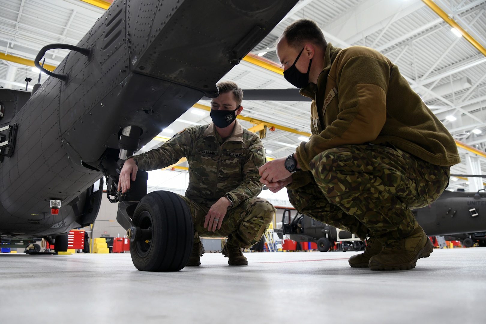 U.S. Army Sgt. Zach Hollman, UH-60 crew chief, Company B, 147th Aviation Regiment, Michigan Army National Guard (MIARNG), and Latvian Air Force Capt. Raimonds Lugēņins inspect landing gear on a Black Hawk Dec. 1, 2021, at Grand Ledge, Mich. The MIARNG is providing training for the first Latvian UH-60 maintainer after the country purchased four Black Hawk helicopters.