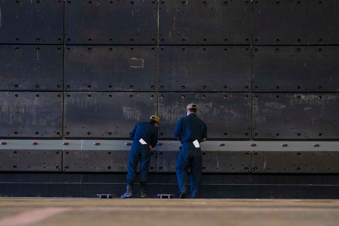 Two sailors paint a ship.