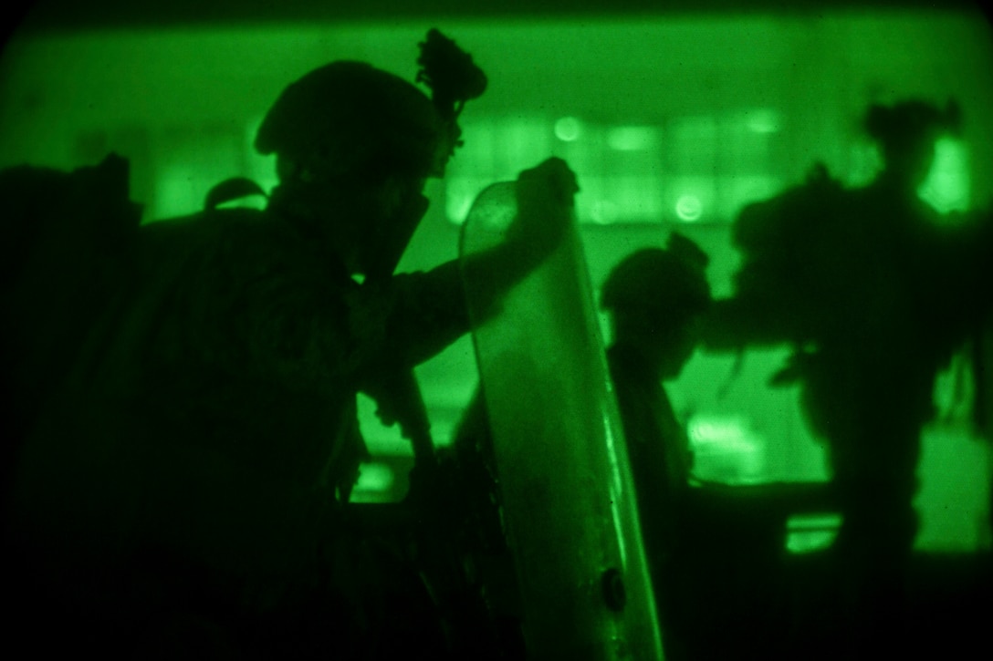 A Marine in silhouette holds a shield illuminated by green light.