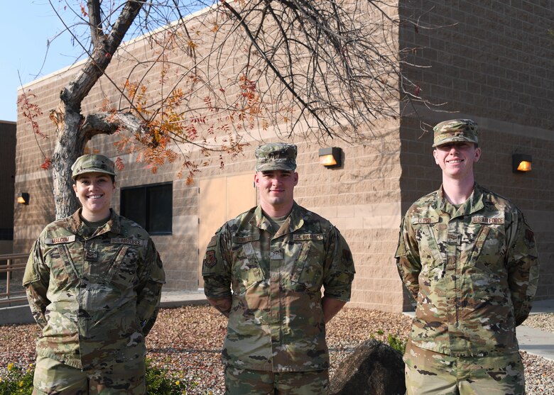 Three service members, a female and two males, wearing the operational camouflage pattern, stand in front of a building facing front