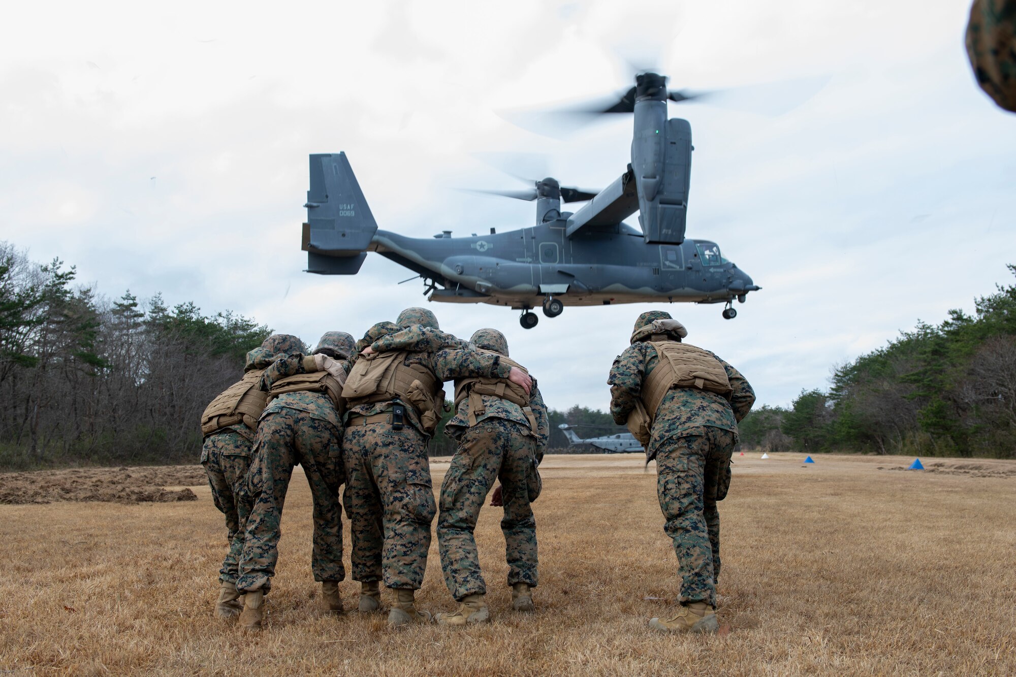 Five U.S. Marines huddle together against the wind generated by a helicopter taking off.