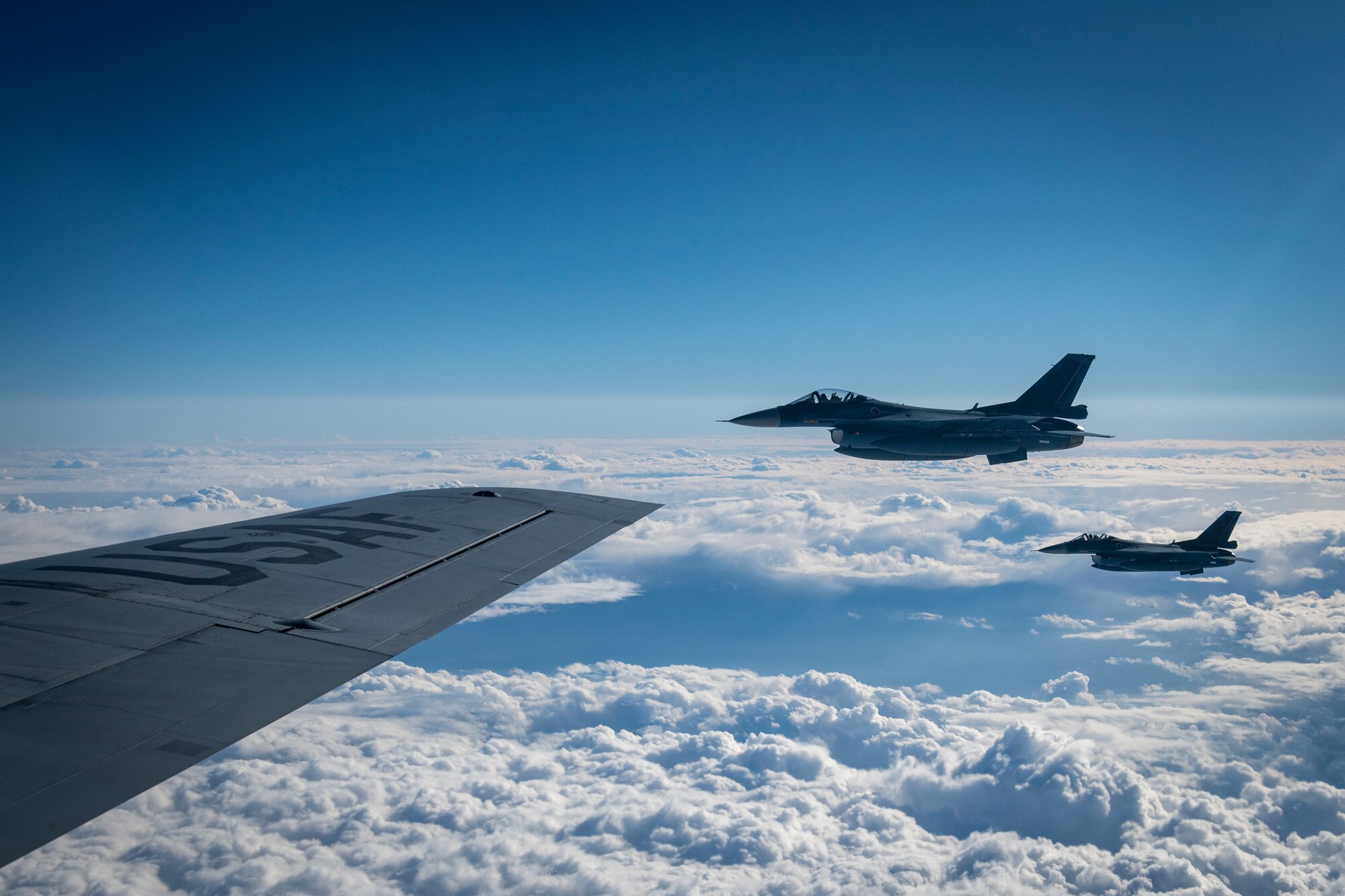 Two F-2 aircraft fly near the wing of a KC-135R Stratotanker.