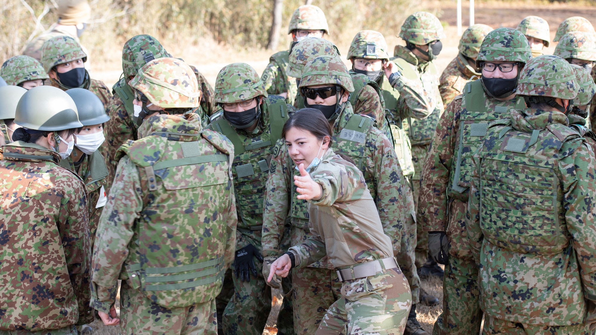 A female pilot translates helicopter safety directions with gestures to Japanese soldiers.