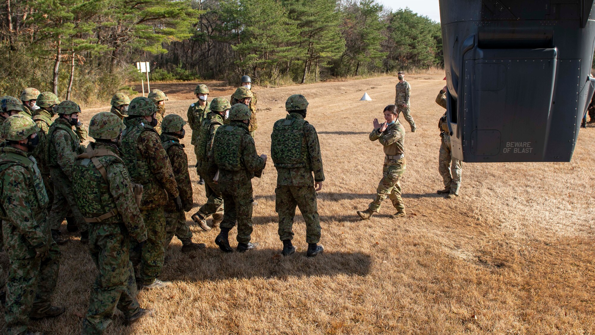 A female pilot translates helicopter safety directions with gestures to Japanese soldiers.