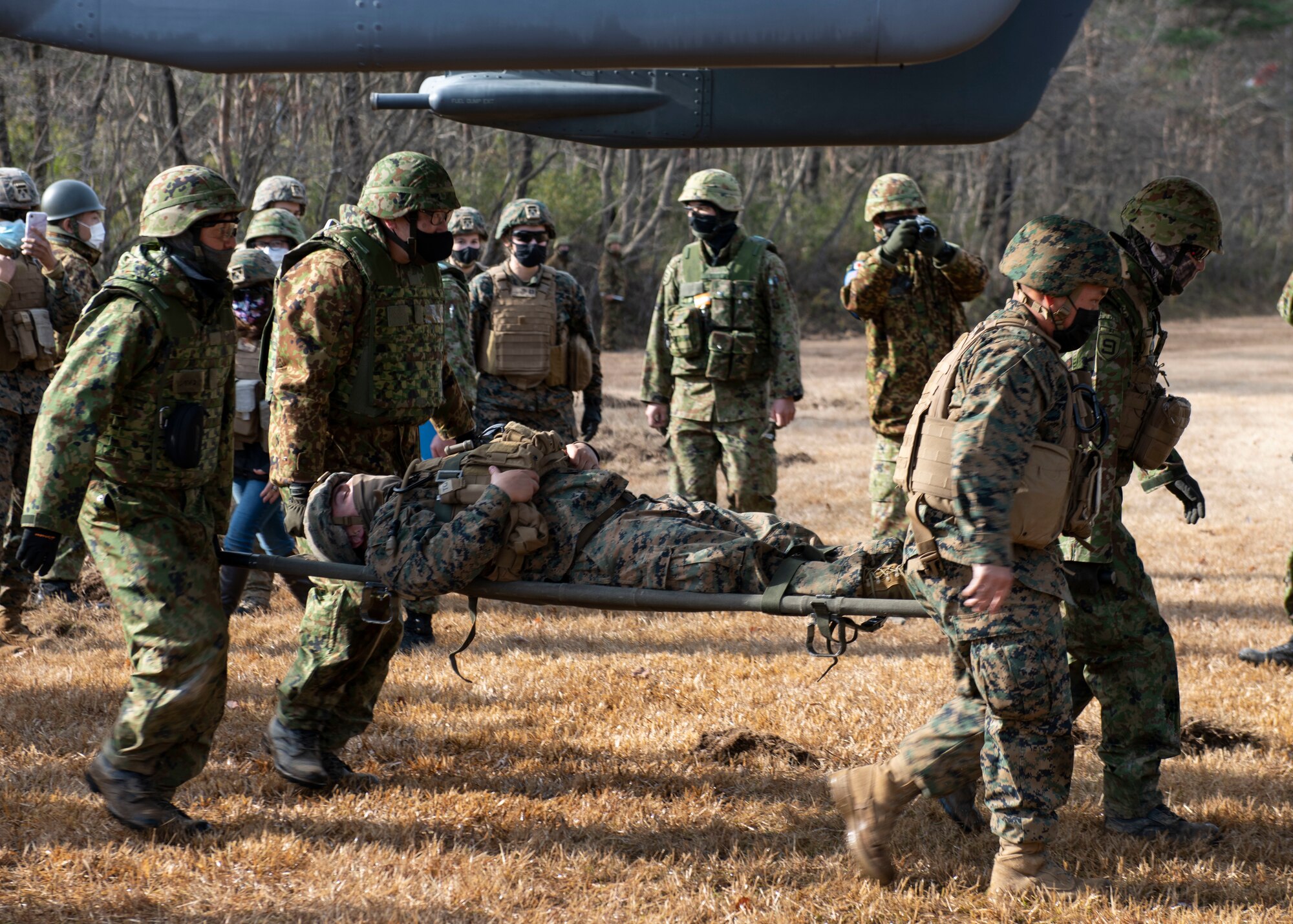 U.S. Marines and Japanese soldiers carry a soldier on a stretcher into a helicopter.