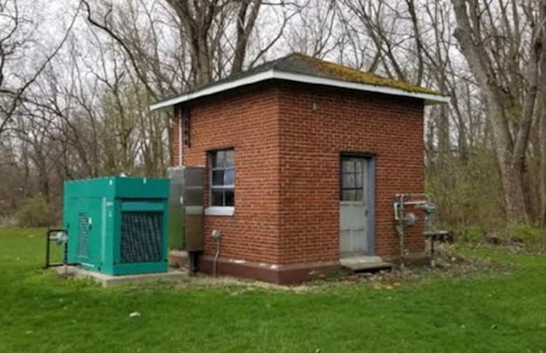 Small red brick building and green generator on green grass