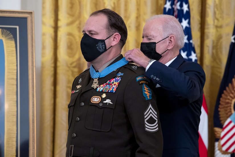 President Joe Biden puts a medal on a soldier's uniform.
