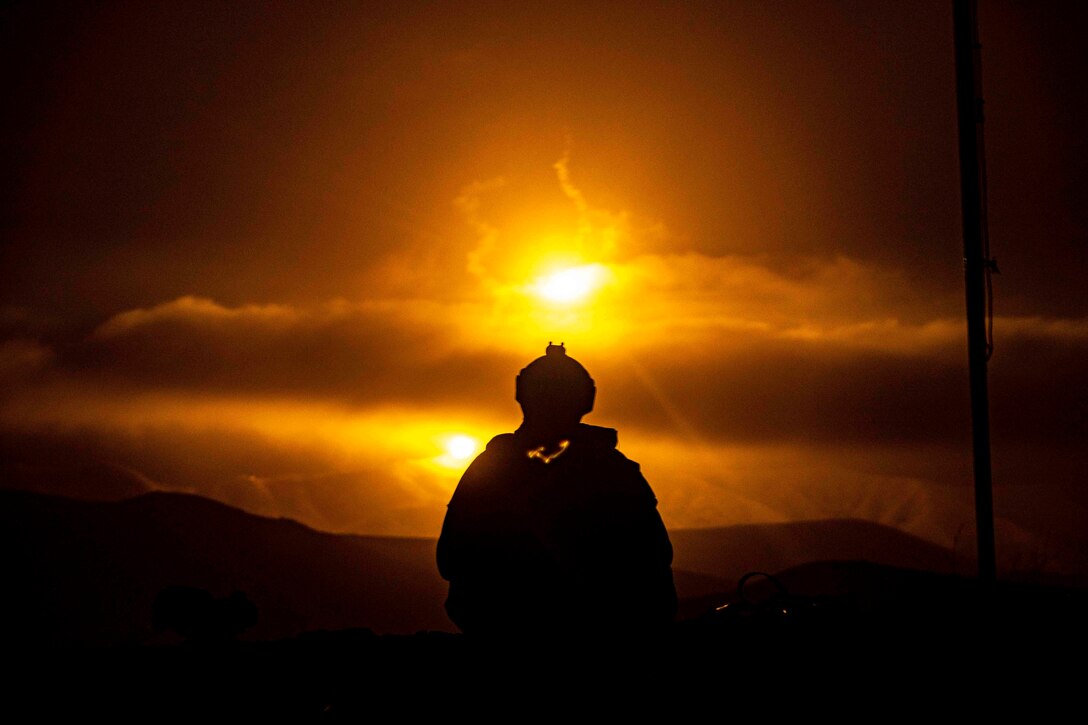 A Marine shown in silhouette as flares illuminate a dark sky.