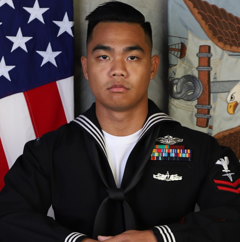 A sailor in dress uniform poses for a photo.