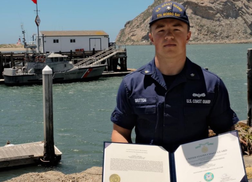 A man holding a paper award poses in front of a waterway.