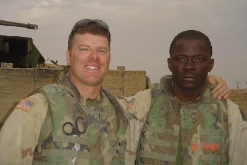 A male service member has his arm around the shoulder of another male service member.