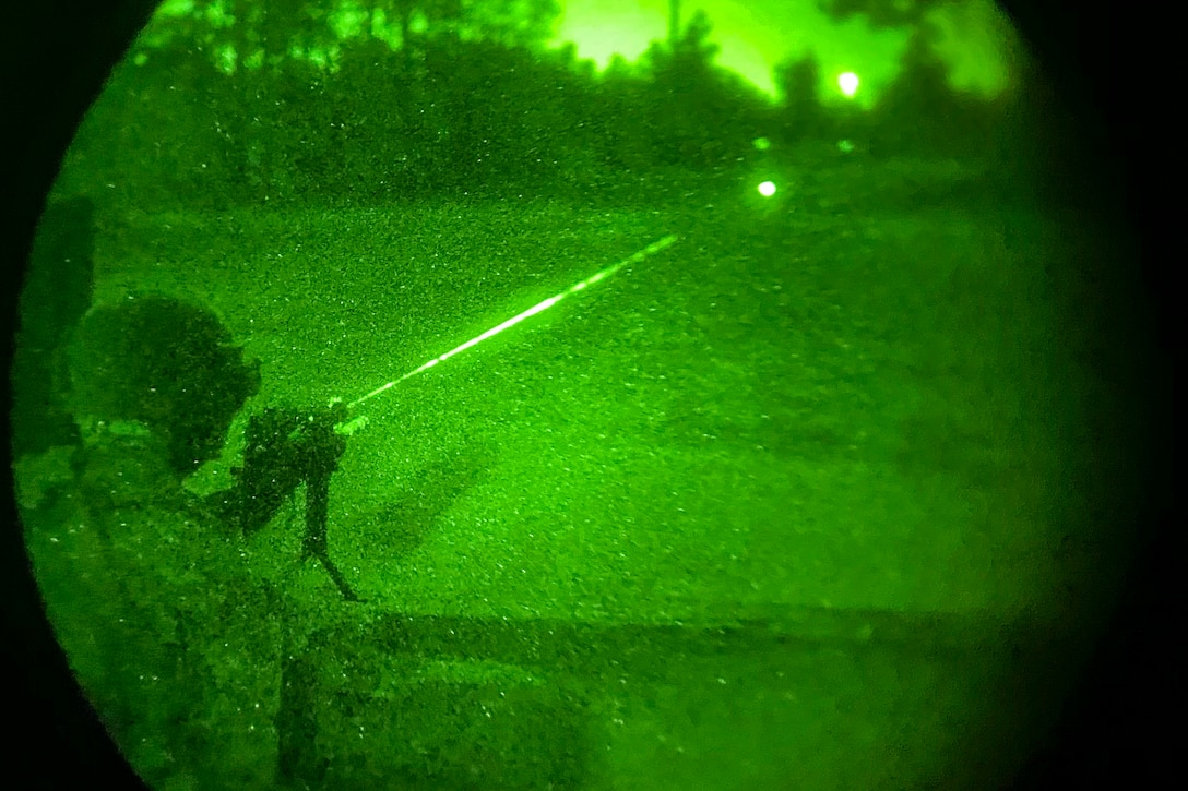 A soldier fires a weapon at a target as seen through night vision goggles.