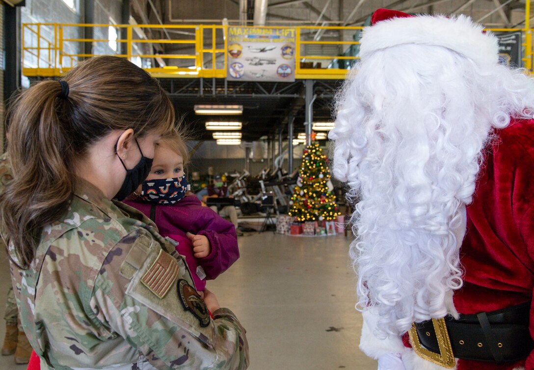 Maj. Debora Berg, 436th Contracting Squadron commander, holds her daughter Mikayla, as Santa Claus greets them at Operation Feed the Troops on Dover Air Force Base, Delaware, Dec. 14, 2021. OFTT volunteers served a traditional holiday meal to more than 900 Team Dover members. (U.S. Air Force photo by Roland Balik)